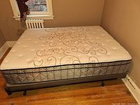 Queen size mattress on bed frame with visible floral embroidery and tufting.