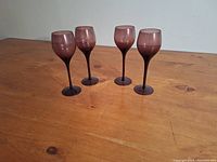 Four purple amethyst wine glasses standing upright on a wooden surface, showing their shape and color.