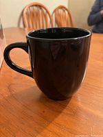Single black coffee mug on wooden table with chair backs in the background