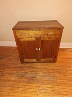 Front view of small wooden hutch showing two drawers with recessed handles and two doors with white round knobs.