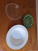 Top down photo showing four stacked white ceramic plates, clear glass bowl with pouring spout, and one green iridescent petal-edged glass dish