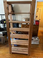 Front view of tall wooden shelf unit showcasing six slatted shelves and solid wooden frame.