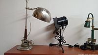 Three different collectible lamps: vintage adjustable metal desk lamp, black studio spotlight on tripod, and decorative green and gold lamp on base.