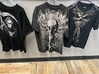 Front view of three black t-shirts with different skeleton-themed graphics, showing designs of Grim Reaper, skull with tree branches, and skeleton face.