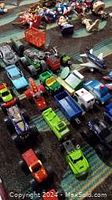 Overhead photo showing a large selection of toy trucks, cars and Transformers figures arranged on a dark fabric surface