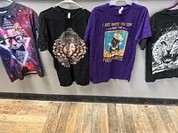 Four cat-themed graphic t-shirts hanging on hangers showing design and color variety