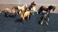 Six collectible horse figurines arranged on dark carpet, showing four horses with painted manes and two with hair manes including one with rider accessory.