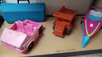 Photo showing pink Barbie truck, orange dump truck, colorful boat with trailer, and blue Gabriel Erector set case in background.
