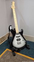 Front full view of electric guitar on stand showing black and silver gradient body, maple neck, and hardware details.