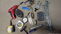 Top view showing all tools spread on the floor, including cordless drill, tape measures, pliers, knives, wrench, metal wire rods, measuring wheel, and accessory bits.