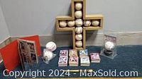 Photo showing a wooden cross wall hanging embedded with baseballs, two loose baseballs, a booklet or album, and multiple stacks of trading cards.