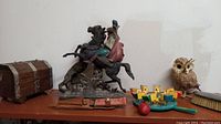 Photo showing the wooden treasure chest, metal statue, wooden chicken toy, owl figurine, cutlery case, and metal hand brush on a shelf