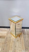 Full view of the rectangular mirrored gold pedestal stand on wooden floor showing mirrored panels and gold trim.