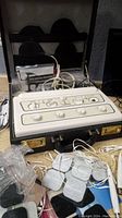 Full view of the Tamex electro therapy device in black attache case, various electrode pads and cables surrounding it, plastic bag of self-adhering electrodes noted.