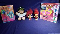 Wide shot showing unopened Trolls Hands Down game, large pirate cabbage patch style troll doll, two small red-haired Troll dolls, and unopened Monopoly Junior Trolls World Tour game.