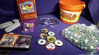 Full overview of all items: Simpsons DVD box, metal rings, Slinky Junior package, Drop in the Bucket bucket with marbles, Harley-Davidson card tin, and assorted tokens.