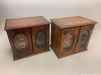 Pair of vintage wooden jewelry boxes with glass oval windows and wooden decorative accents on front doors.