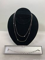 Two layered sterling silver necklaces displayed on black velvet necklace stand with Dyadema bracelet in original box below