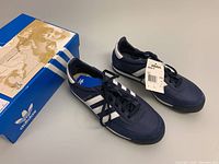 Pair of navy blue Adidas Orion TF running shoes placed next to the original Adidas box showing front angle and tags attached.