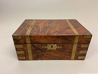 Front view of walnut writing box showing brass straps, keyhole escutcheon, and rich wood grain.