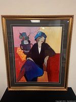 Full view of the framed print showing seated woman in blue hat and black jacket with red chair and floral background.