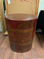 Front view of oval wooden rice barrel with red and gold floral hand-painted design and metal bands around the circumference.