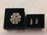 Photo showing the brooch/pendant and the pair of earrings in black jewelry boxes.