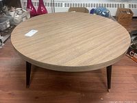 Photo of the round coffee table angled from side showing wood grain laminate top and tapered black metal legs with brass caps.