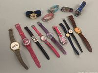Full view of eleven assorted vintage character watches arranged in two rows on a white surface. Various band colors and materials featured.