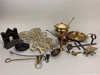 Full overview of vintage brassware and other metal antiques including oil can, fly-shaped ashtray, candlestick, trivets, spoon, and figurine.
