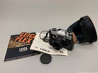 Camera body mounted with Summicron-R lens, manuals, lens cap, and leather case arranged