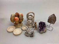 Full lot overview showing all included items: marble egg set on brass stand, carved stone sculpture, pyrite specimen, amethyst geode cluster, smoky quartz on stand, marble dishes, and another small carved stone object.