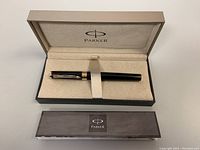 Closed Parker branded box containing the black fountain pen inside beige velvet-like interior with strap securing the pen.