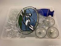 Photo showing clear crystal stemware, round stained glass wall art with birds, and part of the cobalt blue vase