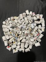 Overhead photo showing a large pile of white ceramic thimbles with colorful designs scattered on a black surface