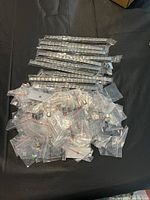 Overview of 10 segmented silver-tone bracelet bands arranged horizontally with approximately 97 individual charm links in small plastic bags below them on a black surface.