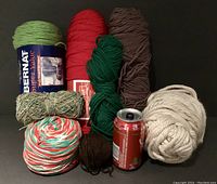 Photo showing multiple skeins and balls of yarn in various colors and sizes, including green, red, brown, and multicolor cotton yarns.