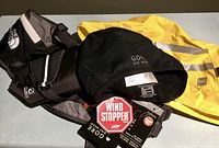 Photo showing three items: MEC yellow bike helmet cover with reflective strips, Gore Bike Wear black helmet cap with tags, North Face black running belt with zippered pouch.