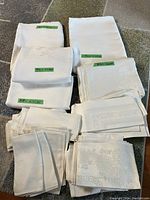 Photo showing multiple folded white linens including tablecloths and napkins with size tags for some items.