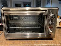 Front view of stainless steel Hamilton Beach countertop oven with handle and windowed door. Three control knobs on the side.