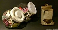 Two round clear containers filled with various matchbooks alongside an antique white metal match dispenser.