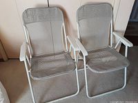 Two folding outdoor chairs with white metal frames, white plastic armrests, and gray plastic mesh fabric seat and backrest placed side by side.