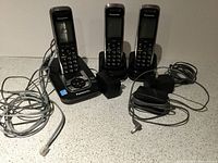 Full view of the phone system showing base station with one handset docked and two handsets on their chargers, with cables visible.