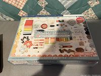 Photo of unopened 1000 piece quilting themed puzzle box labeled 'Thimble Blossoms' by Stitched Puzzles, colorful quilting related images on cover