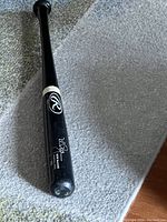 Black Rawlings wooden baseball bat with signature on the barrel area, photographed from above lying on carpet.