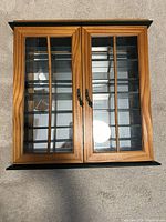 Front view of solid wood wall cabinet with closed double glass-paned doors, showing the wood and glass construction and metal handles.