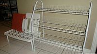 Photo showing two white wire shoe racks with multiple shelves, displayed on a tiled floor in a room corner.