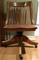 Front view of vintage oak swivel office chair with wooden slat backrest and curved seat
