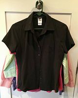 Black short sleeve North Face blouse hung on hanger with other blouses behind it.
