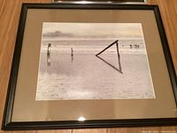 Front view of the larger black and white framed photo showing beachscape with wooden posts and water reflection.